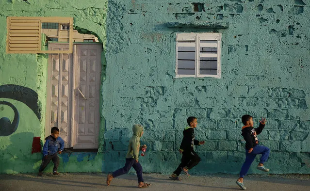In this Saturday December 19, 2015 file photo, Palestinian boys run by a painted house in the Shati Refugee Camp in Gaza City. Shati has always been a symbol of poverty, a grey concrete jungle with 87,000 people packed into one fifth of a square mile (half a square kilometer). But now, overlooking the sewage-contaminated Mediterranean beachfront, the camp's houses are covered in vibrant colors. (Photo by Hatem Moussa/AP Photo)