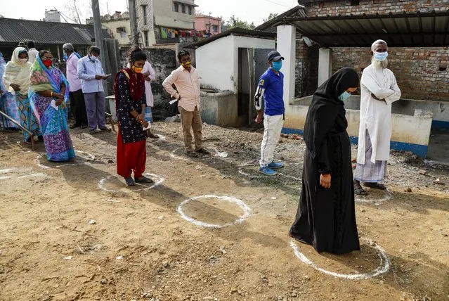 Voters stands on marked areas maintaining social distance as they wait to cast their votes at a polling booth during first phase elections in West Bengal state in Salboni, India, Saturday, March 27, 2021. Voting began Saturday in two key Indian states with sizeable minority Muslim populations posing a tough test for Prime Minister Narendra Modi’s popularity amid a months-long farmers’ protest and the economy plunging with millions of people losing jobs because of the coronavirus pandemic. (Photo by Bikas Das/AP Photo)