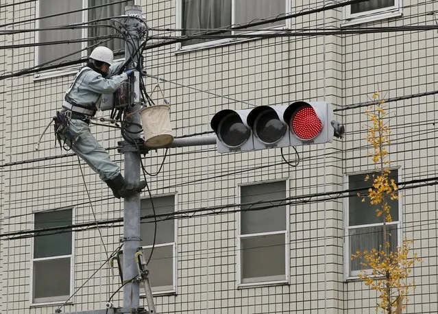A worker climbs a power pole in Tokyo, Japan, December 8, 2015. Japan's government hopes that raising the minimum wage will 'trickle up' into a broader rise in pay and consumption, but the smaller businesses who account for most Japanese jobs are in no shape to square that virtuous circle. Picture taken December 8, 2015. (Photo by Toru Hanai/Reuters)