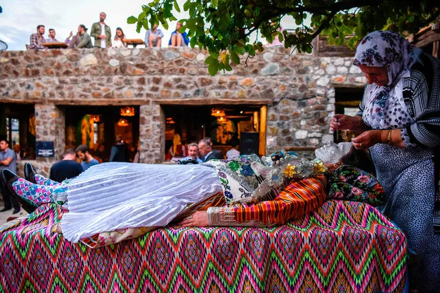 Kosovar woman Sheqerie Buqaj lays on her back on September 5, 2018 as she receives a traditional face painting by Kosovar Bosnian woman Aziza Sefitagic, while presenting the traditional wedding of Bosnian women from Zhupa region, during the “Etno Fest” festival in the village of Kukaj. As part of the centuries old tradition, old ladies prepare young brides, painting their faces in many layers of colors while the golden circles symbolize the cycles of life. Today, this tradition is at the verge of extinction as only a 70 year- old Lady Aziza, continues preparing young brides according to the tradition. (Photo by Armend Nimani/AFP Photo)