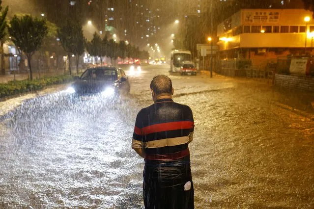 A man stands in the middle of a flooded road, attempting to get the attention of the bus driver during heavy rain, in Hong Kong, China on September 8, 2023. (Photo by Tyrone Siu/Reuters)