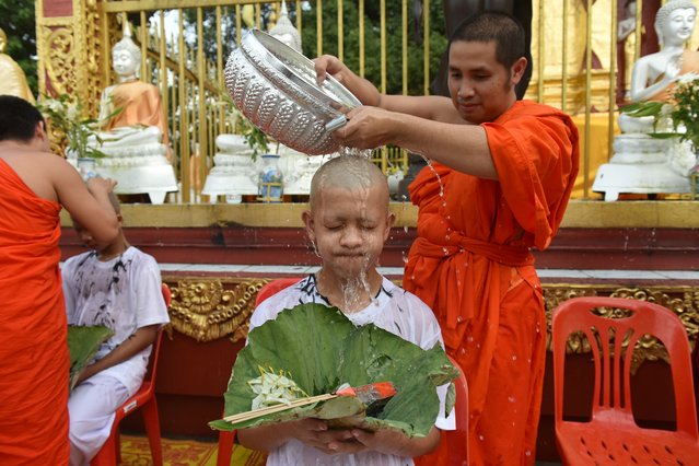 A Buddhist monk bathes the shaved head of the rescued Thai boy and a member of “Wild Boars” football team together with their coach at the Phra That Doi Wao Buddhist temple in the Mae Sai district of Chiang Rai province, Thailand during the religious ordination ceremony on July 24, 2018. Thai boys rescued from deep inside a flooded cave in a dramatic mission had their heads shaved on July 24 before a Buddhist ordination ceremony in honour of a diver who died during the operation. (Photo by Panumas Sanguanwong/AFP Photo)