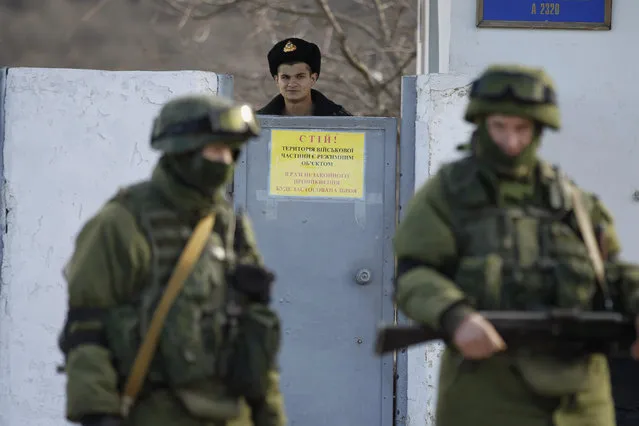 A Ukrainian soldier looks at military personnel, believed to be Russian servicemen, outside the territory of a Ukrainian military unit in the village of Perevalnoye outside Simferopol March 3, 2014. (Photo by Baz Ratner/Reuters)