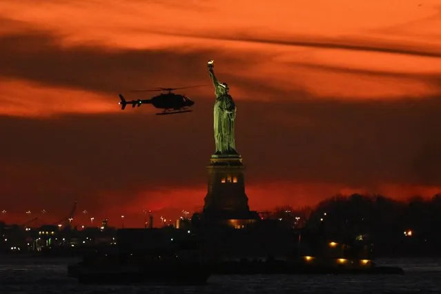 A helicopter flies past the Statue of Liberty at sunset in New York on November 30, 2023. (Photo by Angela Weiss/AFP Photo)