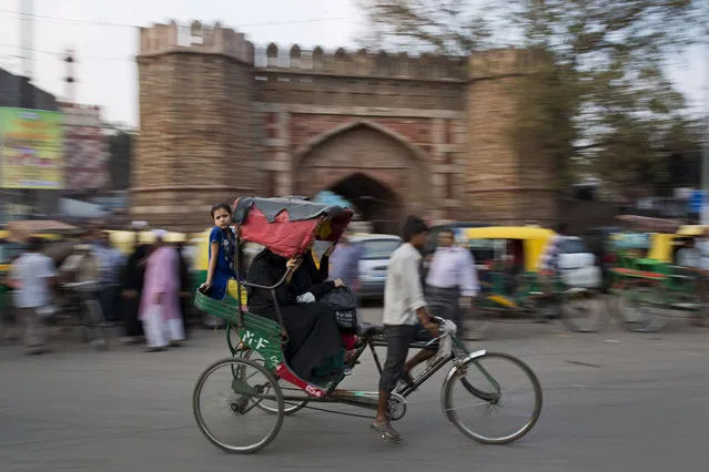 An Indian girl balances herself on the edge of a rickshaw moving past the historic Turkman Gate in the old Delhi area of New Delhi, India, Tuesday, April 14, 2015. The four-century-old neighborhood is chaotic and crowded, yet is the vibrant heart of the city. (Photo by Bernat Armangue/AP Photo)