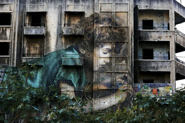 In this November 12, 2018, photo, graffiti by Cuban-American artist Jorge Rodriguez-Gerada depicting a boy is painted on a bullet riddled building on the former frontline of the 1975-1990 Lebanese civil war in downtown Beirut, Lebanon. Nearly 30 years after civil war guns fell silent, dozens of bullet-scarred, shell-pocked buildings are still standing _ testimony to a brutal conflict that raged for 15 years and took the lives of 150,000 people. (Photo by Hassan Ammar/AP Photo)