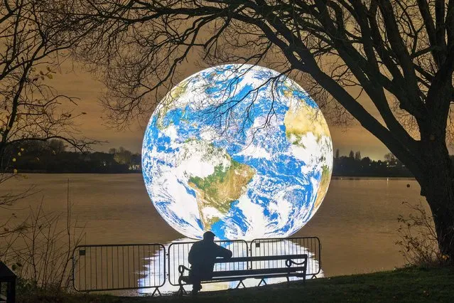 People view artist Luke Jerram's new “Floating Earth” Debuts In Wigan on November 18, 2021 in Wigan, England. The floating Earth will hover over Pennington Flash for 10 days from November 19, as part of a celebration of Wigan and Leigh's watercourses. It is the first time one of Jerram's globes has been floated on an open expanse of water. (Photo by Christopher Furlong/Getty Images)