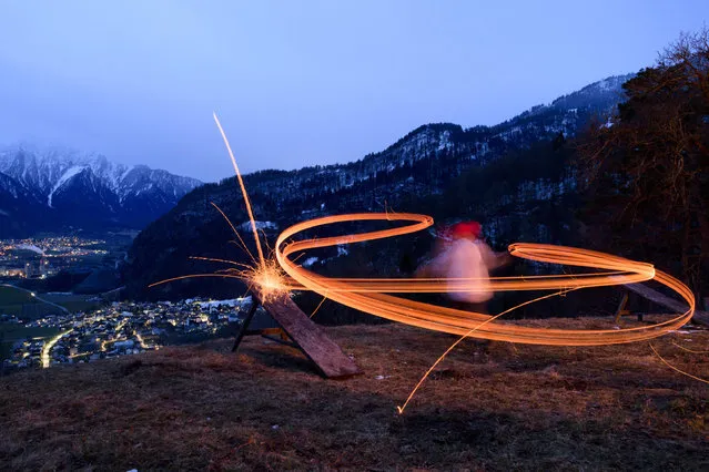 In this March 5, 2017 photo, a boy swings a glowing wooden disc, in Untervaz. Switzerland. Boys throw  glowing wooden discs  with a swing into the valley. The disc is dedicated to someone. (Photo by Gian Ehrenzeller/Keystone via AP Photo)