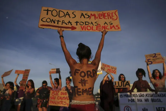 A woman with her body painted with the Portuguese message “Get out Temer”, referring to Brazil's President, holds up a sign that says: “All the women against all violence” during a protest on International Women's Day in Brasilia, Brazil, Wednesday, March 8, 2017. (Photo by Eraldo Peres/AP Photo)