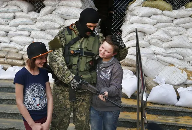 Armed Pro-Russian man poses for a photo with local children next to barricades in front of city hall in Slovyansk, eastern Ukraine, Monday, April 21, 2014. The self-proclaimed mayor of Slovyansk in eastern Ukraine is appealing to Russia to send in peacekeeping troops after a shootout at a checkpoint near the city manned by pro-Russia insurgents. (Photo by Sergei Grits/AP Photo)