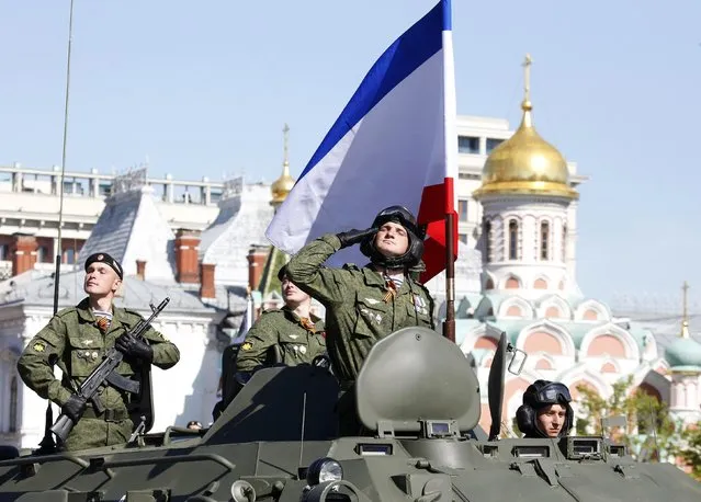 A Russian serviceman aboard an armoured personnel carrier salutes next to the blue-white-red tricolour flag of Crimea, during the Victory Day parade in Moscow's Red Square May 9, 2014. Russia celebrates the 1945 victory over Nazi Germany during World War Two on May 9. (Photo by Grigory Dukor/Reuters)