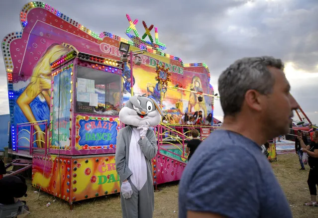 In this picture taken Saturday, September 14, 2019, a person wearing a rabbit outfit stands by a ride at an autumn fair in Titu, southern Romania. Romania's autumn fairs are a loud and colorful reminder that summer has come to an end and, for many families in poorer areas of the country, one of the few affordable public entertainment events of the year. (Photo by Andreea Alexandru/AP Photo)
