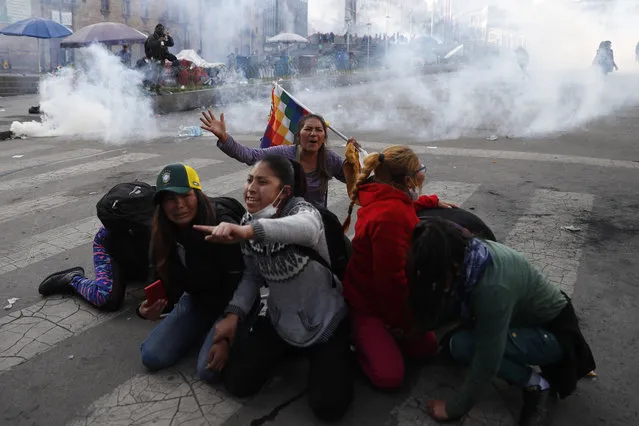 Supporter of former President Evo Morales protect themselves from tear gas launched by the police, in La Paz, Bolivia, Friday, November 15, 2019. Bolivia's new interim president Jeanine Anez faces the challenge of stabilizing the nation and organizing national elections within three months at a time of political disputes that pushed Morales to fly off to self-exile in Mexico after 14 years in power. (Photo by Natacha Pisarenko/AP Photo)