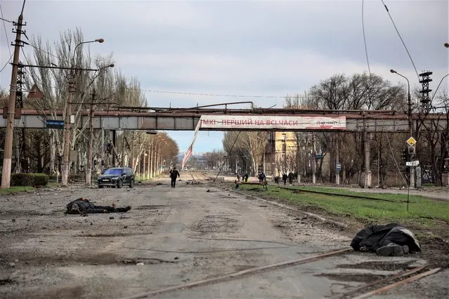 Bodies of civilians lie on the ground as local residents walk past a destroyed part of the Illich Iron & Steel Works Metallurgical Plant, the second largest metallurgical enterprise in Ukraine, in an area controlled by Russian-backed separatist forces in Mariupol, Ukraine, Saturday, April 16, 2022. (Photo by Alexei Alexandrov/AP Photo)