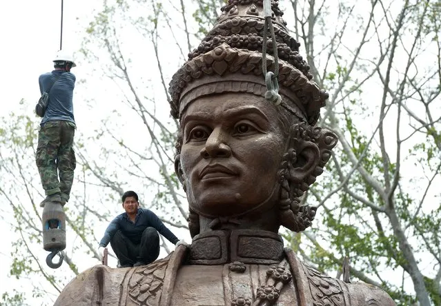 A Thai worker (L) hangs onto a hoisting cable as he and others prepare a statue of King Narai of Ayutthaya for transport from a casting factory in Lopburi province on July 24, 2015. The statue will be part of an installation at a park called Ratchapakdi in Hua Hin to honour past Thai monarchs. (Photo by Pornchai Kittiwongsakul/AFP Photo)