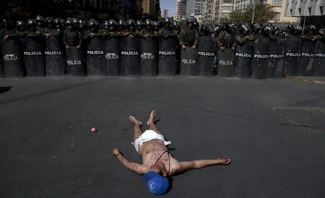A protester demanding an increase in state benefits for people with disabilities, lies before a cordon of police who are serving as a barricade to keep protesters from blocking anymore streets, in La Paz, Bolivia, Thursday, June 2, 2016. Some protesters donned diapers hoping to call attention to disabled people who are demanding their annual state benefits of 1,000 Bolivianos be increased to a monthly stipend of 500 Bolivianos, or about $73 dollars. (Photo by Juan Karita/AP Photo)