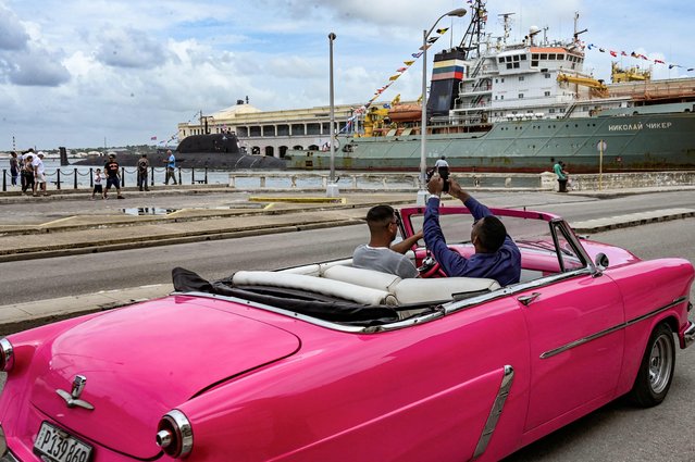 A man takes pictures of the nuclear-powered submarine Kazan (L) and the rescue and salvage tugboat Nikolai Chiker (R), part of the Russian naval detachment visiting Cuba, after its arrival at Havana's harbor on June 12, 2024. The Russian nuclear-powered submarine Kazan – which will not be carrying nuclear weapons – and three other Russian naval vessels, will dock in the Cuban capital from June 12-17. The unusual deployment of the Russian military so close to the United States – particularly the powerful submarine – comes amid major tensions over the war in Ukraine, where the Western-backed government is fighting a Russian invasion. (Photo by Yamil Lage/AFP Photo)