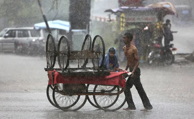 An Indian man tries to protect his child from the pelting rain by covering him with his shirt as he pushes a handcart in Jammu, India, Wednesday, July 12, 2017. The monsoon season in India lasts from June to September is very crucial for India's agriculture sector that accounts for more than 13 percent of the economy and provides work for about half of the country's 1.25 billion people. (Photo  by Channi Anand/AP Photo)