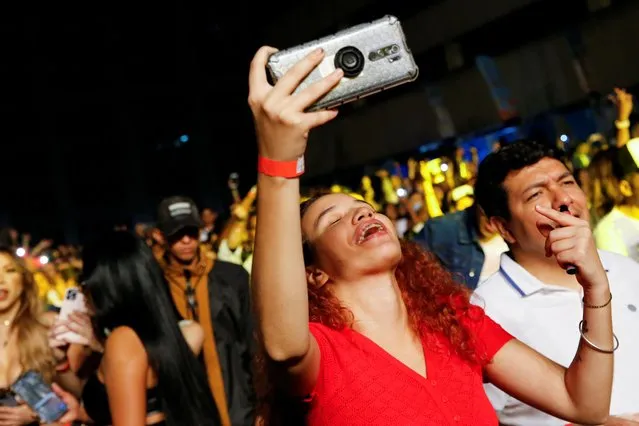 A woman sings while recording with her phone during an urban music festival housed in the open parking lot of a shopping center in Caracas, Venezuela on June 4, 2022. (Photo by Leonardo Fernandez Viloria/Reuters)