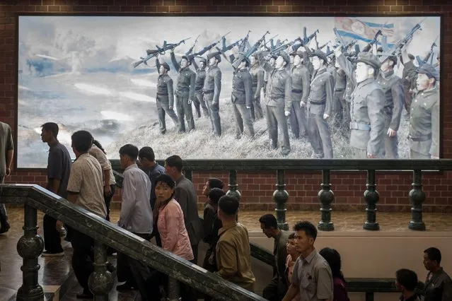 In this photo taken on July 29, 2017, people walk up stairs before a propaganda poster showing Korean People's Army (KPA) soldiers at a museum in Sinchon, south of Pyongyang. (Photo by Ed Jones/AFP Photo)