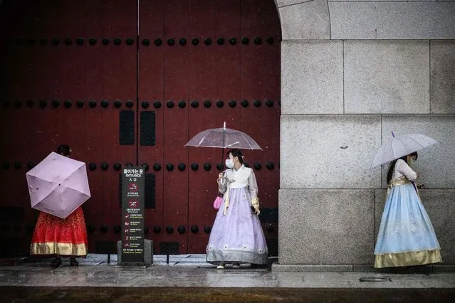 Women wearing traditional Hanbok dresses use umbrellas to shelter from a heavy downpour outside the Gyeongbokgung Palace in Seoul on June 23, 2022. (Photo by Anthony Wallace/AFP Photo)