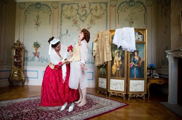A woman is helped into a lace corset in preparation for the Rococo Palace Festival in Frederick field, Berlin, Germany, August 23, 2014. Historical dances and games, concerts and theater performances occur during the festival, which is being held at a castle. (Photo by Joerg Carstensen/EPA)