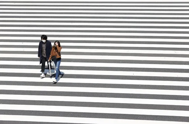 People walk on the crosswalk, downtown, which has less than usual passersby after the state of emergency was announced, following the coronavirus disease (COVID-19) outbreak, in Shinjuku City, Tokyo, Japan, in this photo taken by Kyodo April 11, 2020. (Photo by Kyodo News via Reuters)