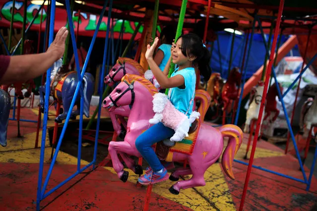 A girl rides a merry go round at a fair during the festivities of El Divino Salvador del Mundo (The Divine Savior of the World), patron saint of the capital city of San Salvador in San Salvador, El Salvador August 2, 2016. (Photo by Jose Cabezas/Reuters)