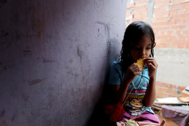 One of Yennifer Padron and Victor Cordova's daughters eats an arepa in the family room of the house that they share at Petare slum in Caracas, Venezuela, August 21, 2017. (Photo by Andres Martinez Casares/Reuters)