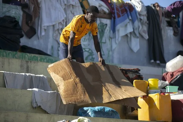 A man dries a piece of cardboard he uses to sleep on at the Hugo Chavez public square transformed into a refuge for families forced to leave their homes due to clashes between armed gangs in Port-au-Prince, Haiti, Thursday, October 20, 2022. (Photo by Joseph Odelyn/AP Photo)