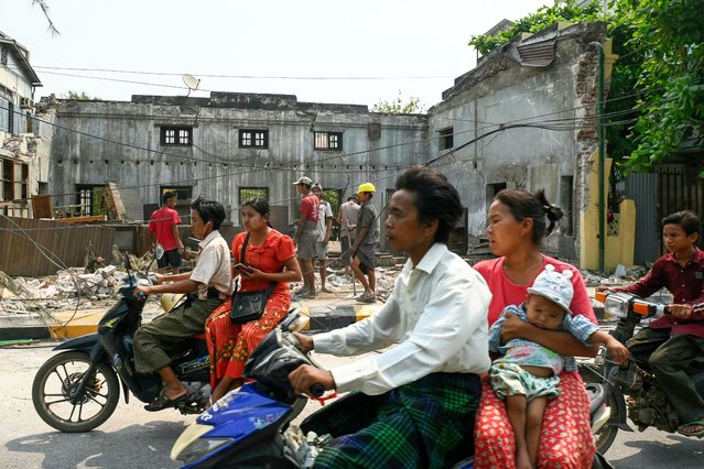 A woman carries a baby as people ride on motorbikes past the rubble of a collapsed building being cleared up workers in Kyaukse Township on April 4, 2025, one week after the March 28 earthquake. The shallow 7.7-magnitude earthquake on March 28 flattened buildings across Myanmar, killing more than 3,000 people and making thousands more homeless. (Photo by Sai Aung Main/AFP Photo)