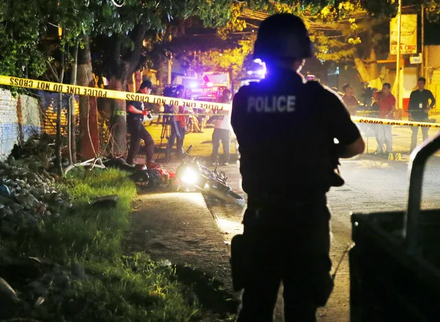 A police SWAT member stands guard as police operatives examine the scene where two bodies lay on a road after being killed in a police drug “buy-bust” operation before dawn Friday, September 23, 2016 in Pasig city, east of Manila, Philippines. Philippine President Rodrigo Duterte said on Thursday he will invite the U.N. chief and European Union officials to investigate his bloody anti-drug crackdown, but only if he can question them in public afterward to prove their human rights concerns are baseless. More than 3,000 suspected drug dealers and users have been killed since July and more than 600,000 others have surrendered for fear of being killed in Duterte's crackdown. Despite growing alarm, Duterte said he won't stop the campaign. (Photo by Bullit Marquez/AP Photo)