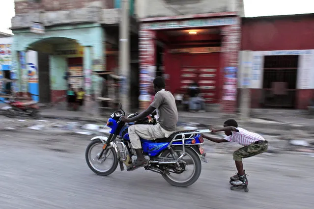 A kid wearing rollerblades hitches a ride via motorbike, in Port-au-Prince, Haiti, Sunday, October 25, 2015. The country held the first-round presidential vote Sunday. Haitians chose between 54 presidential hopefuls and a slew of legislative and municipal candidates. (Photo by Ricardo Arduengo/AP Photo)
