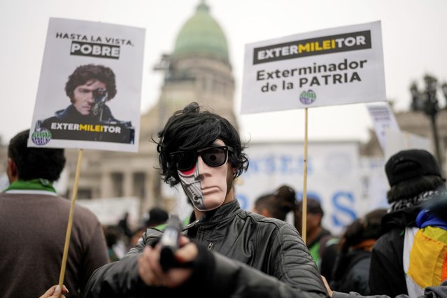 A masked anti-government protester aims a toy gun during a demonstration outside Congress where lawmakers debate a reform bill promoted by President Javier Milei in Buenos Aires, Argentina, Wednesday, June 12, 2024. The sign at right reads in Spanish “Exterminator of the homeland”. (Photo by Natacha Pisarenko/AP Photo)