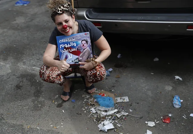 A member of the clown troupe, Clown Me In, holds an Arabic placard that reads, “We are yesterday and today, but tomorrow no, we have a show”, as she poses for a picture next of a pile of garbage, during Lebanon's first national elections in nine years, outside a ballot station in Beirut, Lebanon, Sunday, May 6, 2018. The group said their act is a message to voters to think about the state of the country and the political stagnation of the last nine years. (Photo by Hussein Malla/AP Photo)