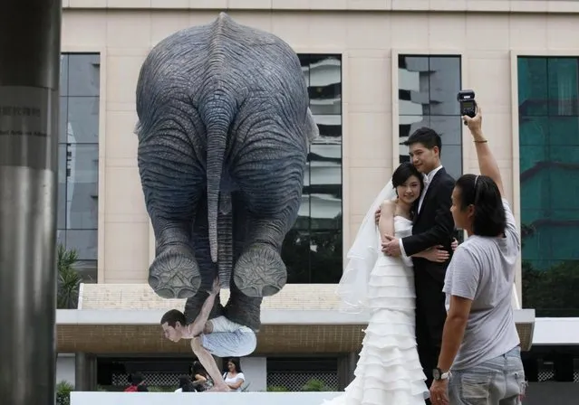 A couple poses for a photo in front of a five meters high sculpture “Pentateuque” created by Contemporary French artist Fabien Merelle in Central, business district of Hong Kong, Tuesday, May 21, 2013. The artwork brings to real life the fantastical and seemingly impossible act of an average man balancing a gigantic elephant. The elephant and the man are modeled on one at the Singapore Zoo and on the artist himself. (AP Photo/Kin Cheung)