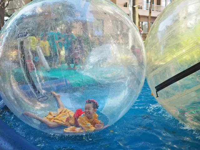 A girl in a kimono laughs as she rides on water in an inflatable plastic bubble at a school fair outside Bangkok, Thailand, Saturday, November 21, 2015. (Photo by Ted Anthony/AP Photo)