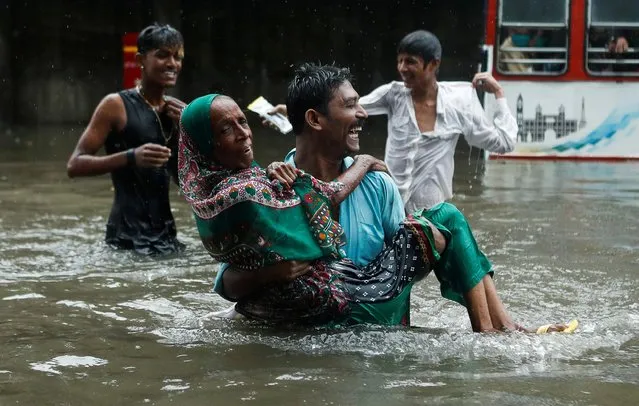 A man carries an elderly woman as they cross a waterlogged street during heavy rainfall in Mumbai, India, July 15, 2020. (Photo by Francis Mascarenhas/Reuters)