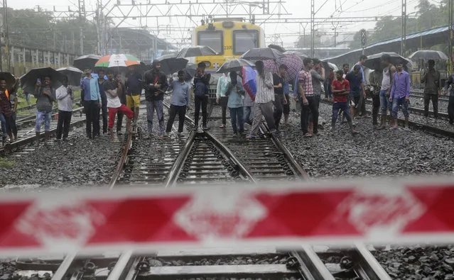 Commuters watch rescuers work at the site of a pedestrian bridge that collapsed at a train station in Mumbai, India, Tuesday, July 3, 2018. Part of a pedestrian bridge at a Mumbai train station collapsed Tuesday morning during heavy rains. The concrete slab fell onto empty train tracks, damaging part of the platform roof and high-tension electric wires. (Photo by Rafiq Maqbool/AP Photo)