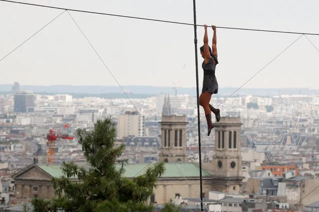 Tightrope walker Tatian-Mosio Bongonga hangs from a tightrope as she pauses while scaling the Monmartre hill towards the Sacre Coeur Basilica (not pictured) in Paris, France, July 20, 2018. (Photo by Philippe Wojazer/Reuters)