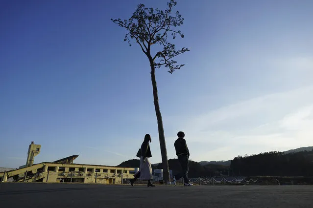 A man and a woman walk near a replica of a lone pine tree that initially survived the 2011 tsunami that flattened the surrounding coastal forest, in Rikuzentakata, Iwate Prefecture, northern Japan Thursday, March 4, 2021. The tree, which eventually died of seawater exposure, was known as the “Miracle Pine”, and townspeople treated, reinforced and then preserved it as a memorial and symbol of hope for the region. (Photo by Eugene Hoshiko/AP Photo)