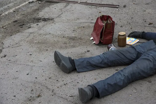 The body of a civilian lies on the ground at a bus stop not far from a destroyed during a heavy fighting part of the Illich Iron & Steel Works Metallurgical Plant, the second largest metallurgical enterprise in Ukraine, in an area controlled by Russian-backed separatist forces in Mariupol, Ukraine, Saturday, April 16, 2022. Mariupol, a strategic port on the Sea of Azov, has been besieged by Russian troops and forces from self-proclaimed separatist areas in eastern Ukraine for more than six weeks. (Photo by Alexei Alexandrov/AP Photo)