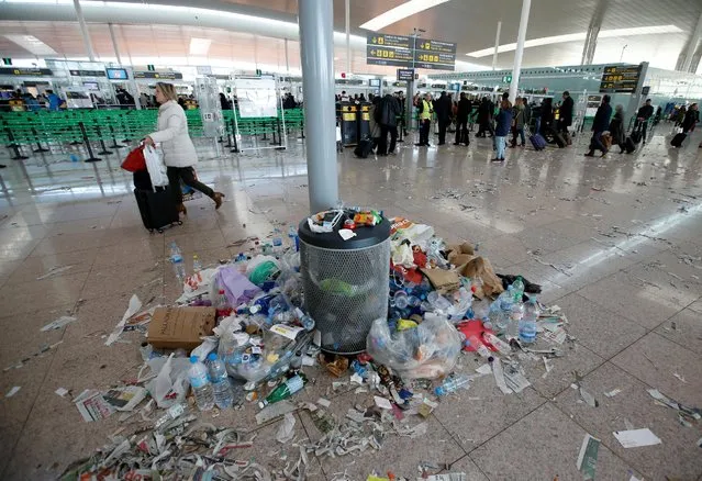 A passenger walks past a bin full of garbage during a protest by the cleaning staff at Barcelona's airport, Spain December 1, 2016. (Photo by Albert Gea/Reuters)