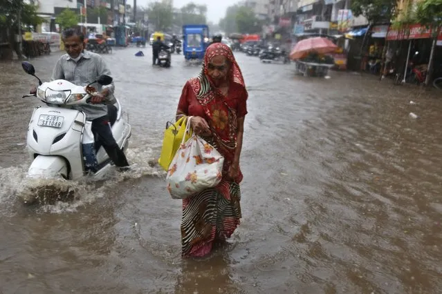 A motorist and a woman wade through a waterlogged street after heavy rains in Ahmedabad, India, Tuesday, May 18, 2021. Cyclone Tauktae, the most powerful storm to hit the region in more than two decades, packed sustained winds of up to 210 kilometers (130 miles) per hour when it came ashore in Gujarat state late Monday. (Photo by Ajit Solanki/AP Photo)