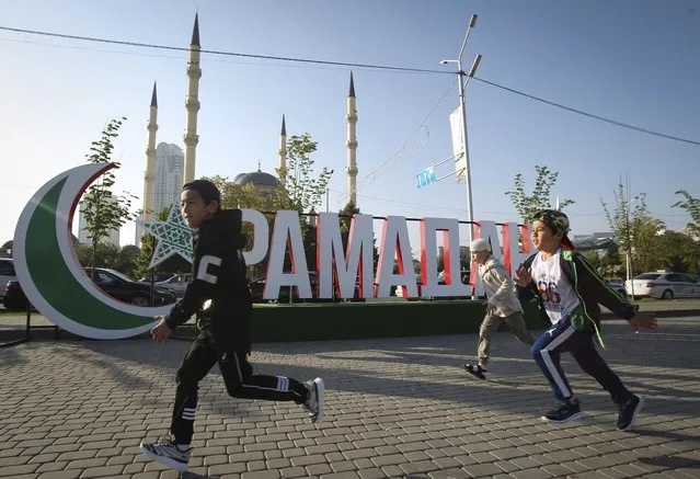 Children run past a sign reading “Ramadan” with the Central Mosque “Heart of Chechnya” in the background during celebrations of Eid al-Fitr holiday, a feast celebrated by Muslims worldwide, in Grozny, Russia, Thursday, May 13, 2021. Eid al-Fitr marks the end of the Muslims' holy fasting month of Ramadan. (Photo by Musa Sadulayev/AP Photo)