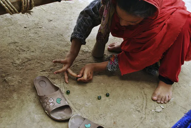 In this Friday, August 10, 2018, photo, in Mardan, Pakistan, Ansa Khan plays marbles on the dirt floor of her home. This is the most famous game in rural areas of Khyebr Pakhtunkhwa Province, which is played by small girls and boys both. (Photo by Saba Rehman/AP Photo)