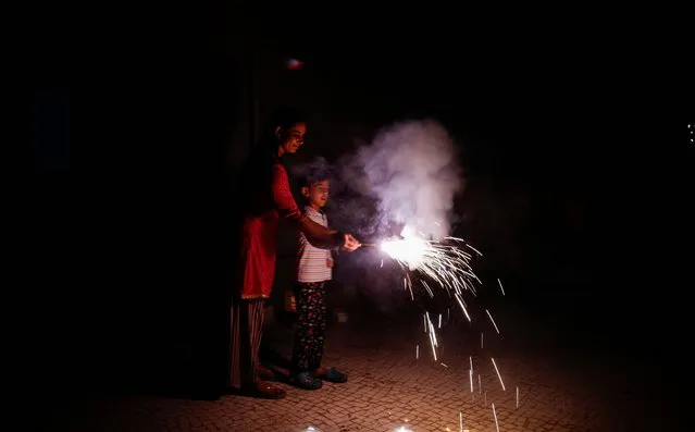 A woman and her son light fireworks to celebrate Diwali, the Hindu festival of lights, in Ahmedabad, India on November 12, 2023. (Photo by Amit Dave/Reuters)