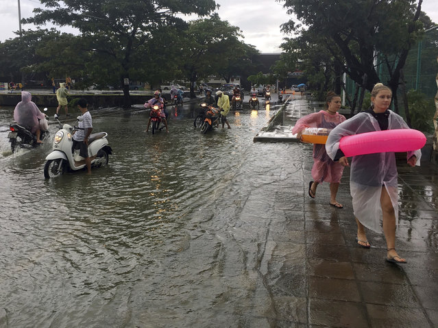 In this Thursday, January 5, 2017 file photo, tourists wear flotation devices while scooter riders pause before crossing a flooded roadway on Ko Samui, Thailand. Authorities say at least 25 people have died in severe flooding in southern Thailand since New Year’s, leaving businesses paralyzed and thousands of tourists stranded. The Interior Ministry said in a report Tuesday that the main highway connecting the south with the rest of the country was swamped. (Photo by Adam Schreck/AP Photo)