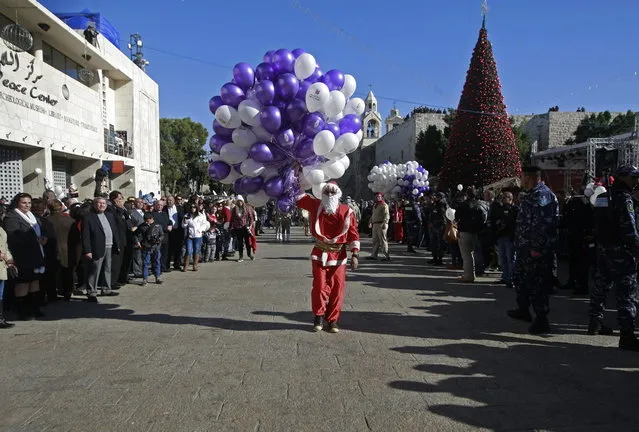 A Palestinian youth dressed as Santa Claus holds balloons at Manger Square, outside the Church of the Nativity, traditionally believed by Christians to be the birthplace of Jesus Christ, in the West Bank town of Bethlehem, Tuesday, December 24, 2013. (Photo by Majdi Mohammed/AP Photo)