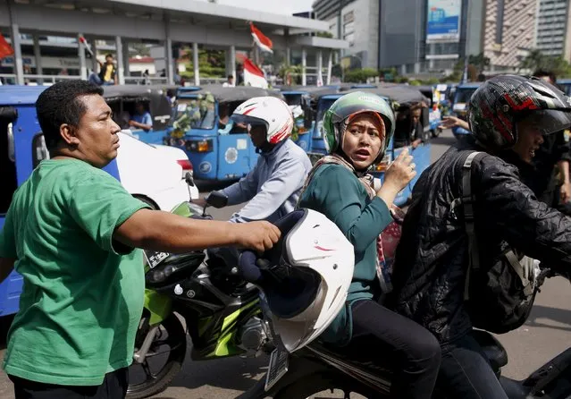 A man strikes a motorcycle taxi driver, carrying a woman passenger with a helmet during a protest rally for ban on online taxi apps in Jakarta, Indonesia March 22, 2016. (Photo by Darren Whiteside/Reuters)